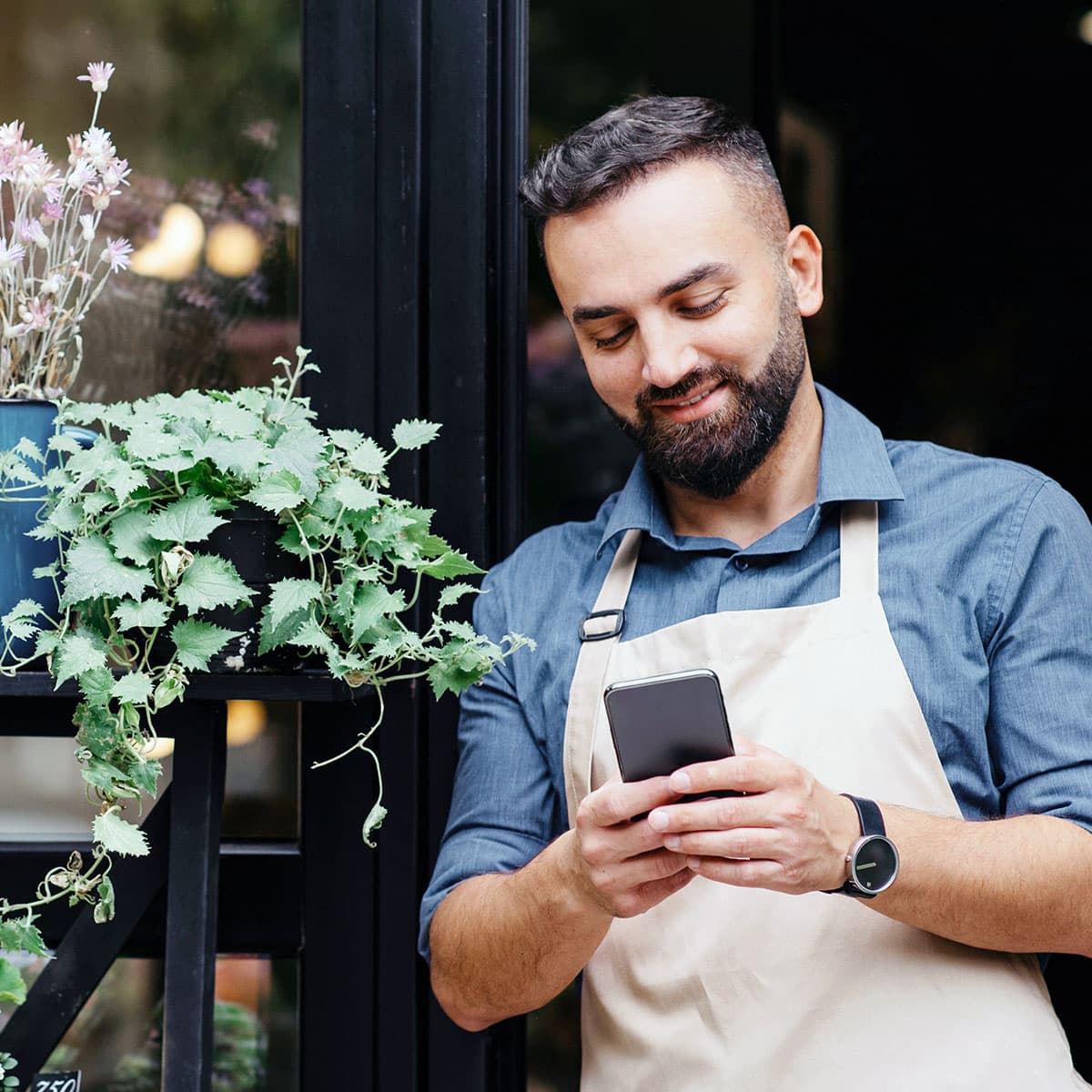 Florist business owner using a smartphone outside their shop